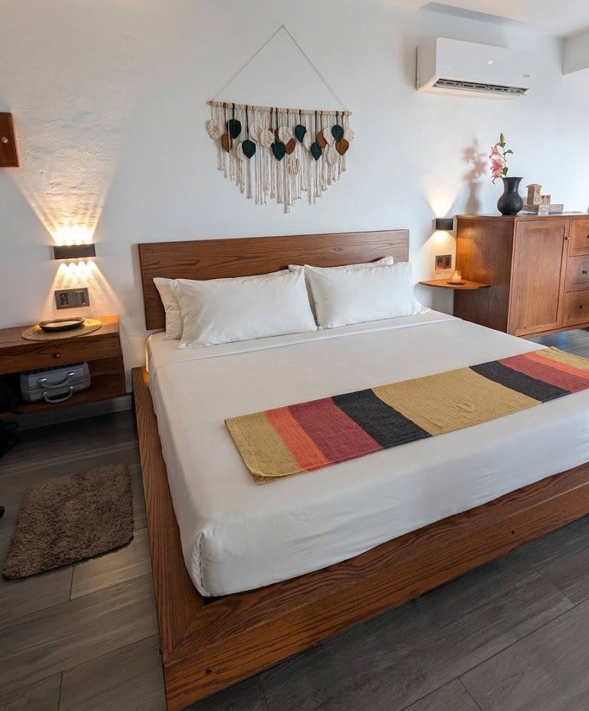 A made bed under a macrame hanging, with reading lamps either side.