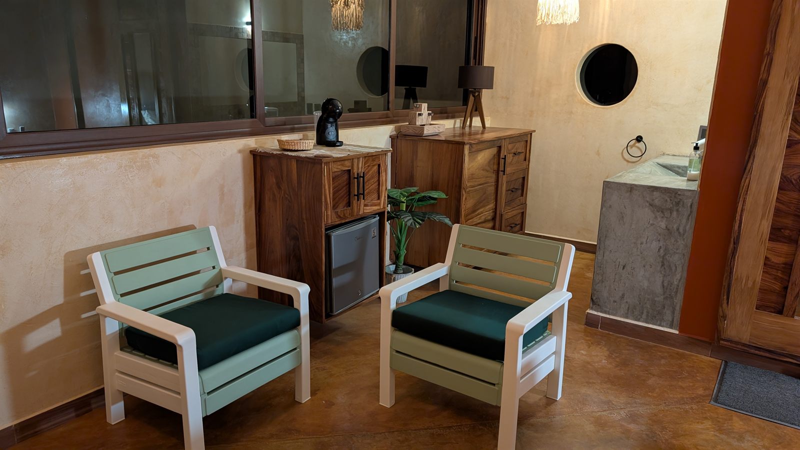 Two green chairs beside a coffee machine and a small fridge.