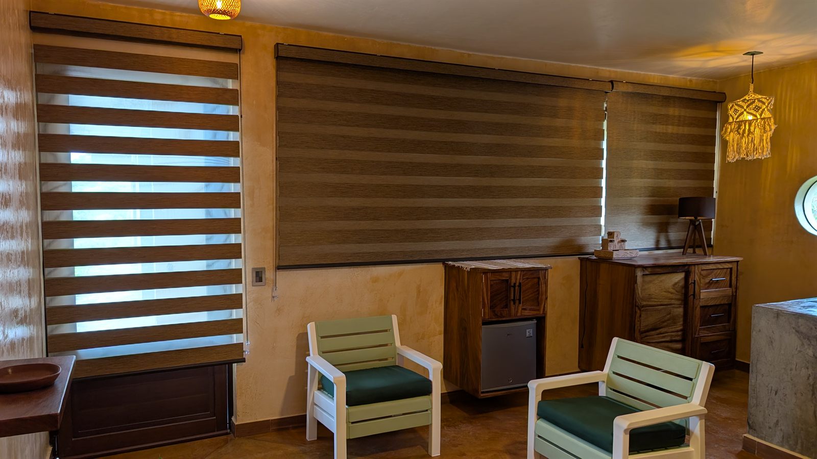 The sitting room with woven blinds half drawn and two green chairs.